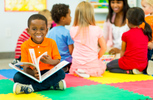 A child reading a book and smiling at the camera