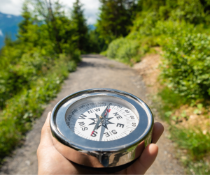 An up close image of a hand holding a compass outdoors in the mountains