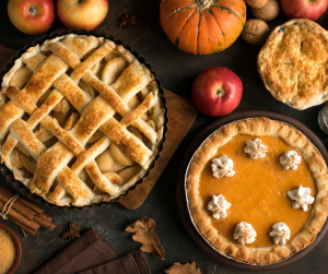 An apple pie and a pumpkin pie lying on a table with apples and pumpkins around them